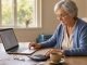 Une retraitée active examine calmement des calculs de pension et de salaire sur un ordinateur, entourée de documents administratifs vierges à une table.